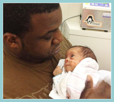 Photo of father and premature baby resting on his chest with both looking directly at each other.