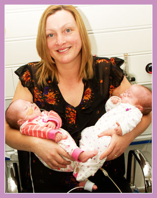 Photo of mother holding her twins, one in each arm